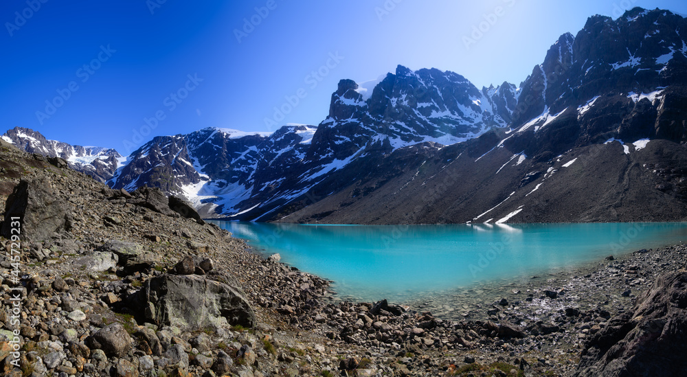 Fabulous blurry panorama of a glacial cold lake under snowy mountains in summer among the stones. Norway trekking.Fabulous view of the blurred calm water and blue sky. summer. Norway journey. Tourism.