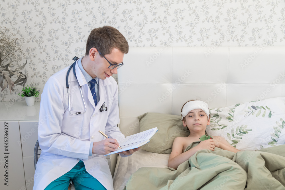 The pediatrician is at the appointment of a sick child. A boy with a thermometer, temperature. The doctor records the result of the examination in a notebook The pediatrician is at the appointment of a sick child. A boy with a thermometer, temperature. The doctor records the result of the examination in a notebook