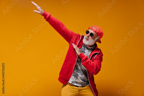 Bild auf Leinwand White bearded man in sunglasses and cap posing on orange background