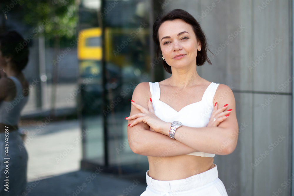 fashionable woman with red manicure and wristwatch folded her arms and looks into the camera on an outdoor glass background. a close-up business portrait