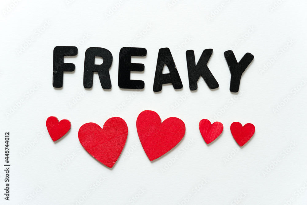 sign with the word freaky in black chalk letters and red, hand painted wooden shapes (hearts) on a white background