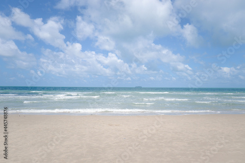 Beautiful natural scene of tropical summer sand beach with blue sea and cloudy sky, ocean waves crashing on beach island. © Stella