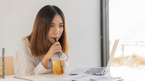 Businesswoman drinking water during work in room with graph papers and laptop on table