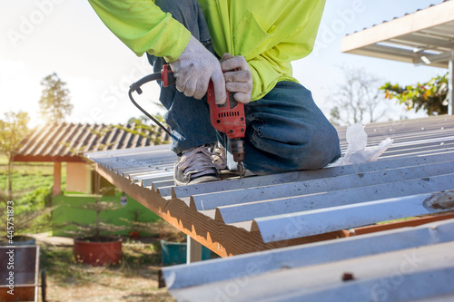 Construction worker wearing safety harness belt during working on roof structure of building on construction site,Roofer using air or pneumatic nail gun and installing concrete roof tile on top roof.