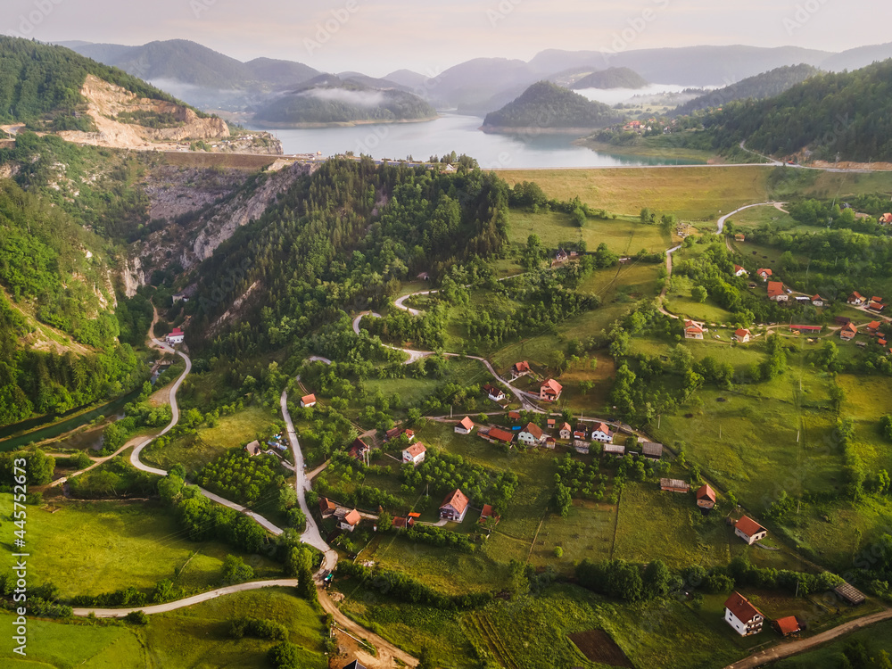 Tranquil view of remote mountain village with lake in misty summer morning. Nature outdoors travel destination, National park Tara, Zaovine lake, Serbia  - obrazy, fototapety, plakaty 