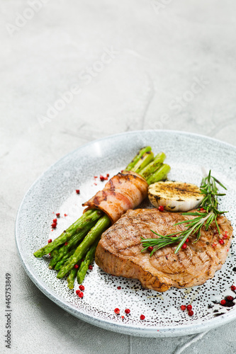 grilled pork steak with asparagus and rosemary leaf on concrete table close up