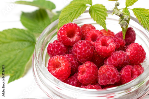 Ripe raspberries in a bowl close-up, Bowl with natural ripe organic berries with green leaves