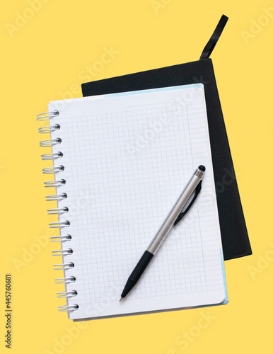 white notebook with clean papers and silver pen on the yellow background	
