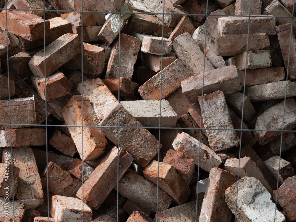 pile of used red bricks behind metal fence pile of used red bricks behind metal fence