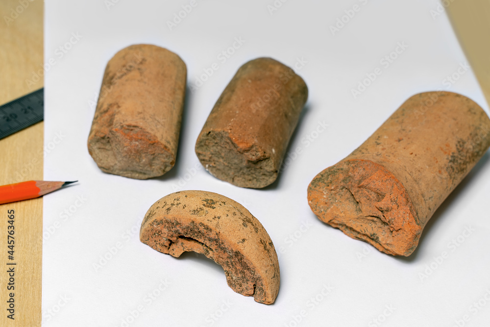 Some peices of clay aged-damaged ceramic artefacts found during the archaeological excavations settled on wooden background with sheets of paper, metallic ruler and pencils. Copy space, close up.