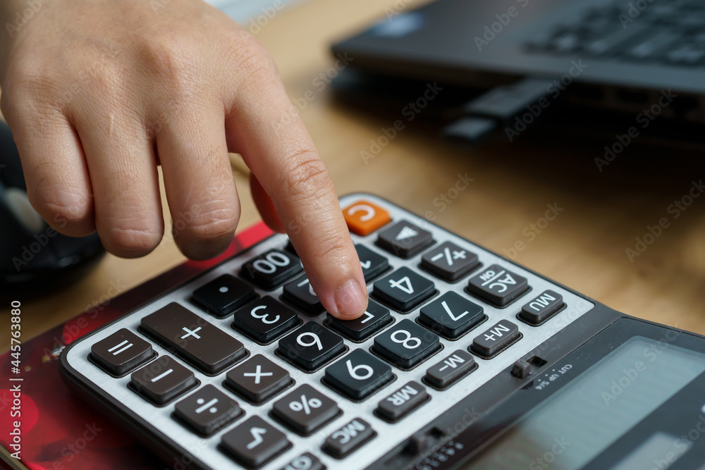 A calculator was placed on the table with a small woman's hand pressing on the keyboard. A calculator was placed on the table with a small woman's hand pressing on the keyboard.