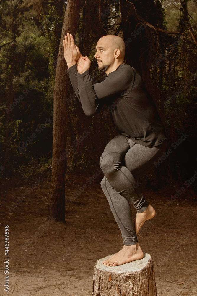 Latin man Instructor practicing yoga on top of a log in the forest, lateral view