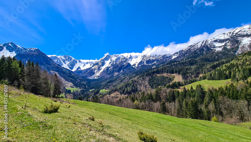 A panoramic view on Baeren Valley in Austrian Alps. The highest peaks in the chain are sonw-capped. Lush green pasture in front. A few trees on the slopes. Clear and sunny day. High mountain chains.