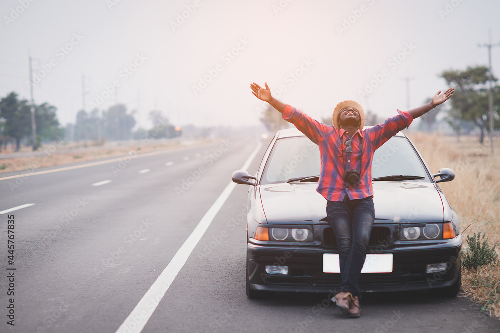 Carefree tourist african man stands on the  highway road with arms outstretched in freedom pose with black car