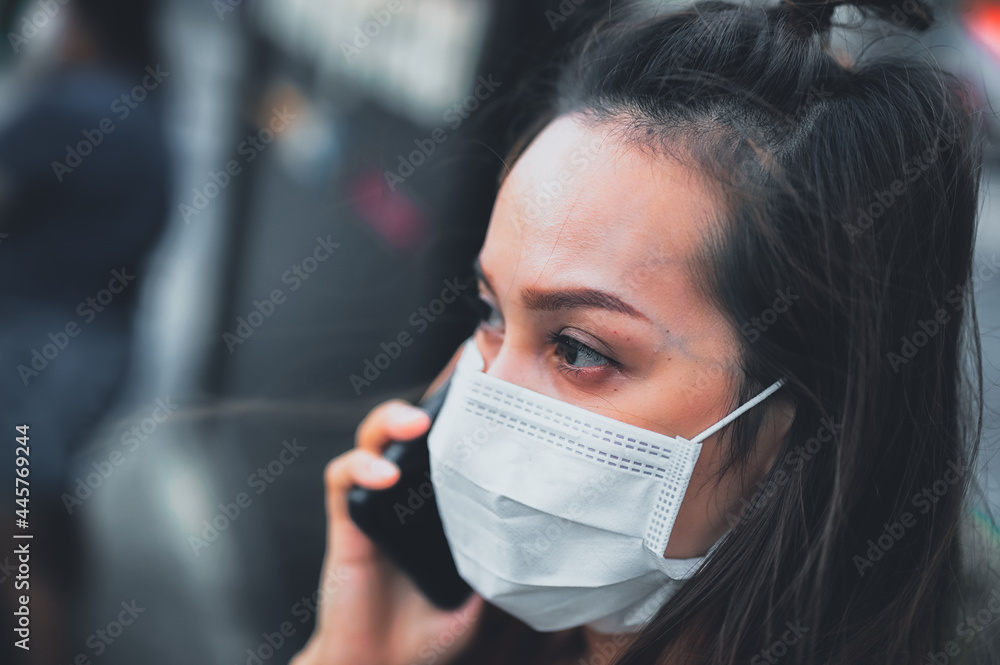 Young woman wearing surgical mask on street while using mobile phone. Portrait of young woman wearing a protective mask to prevent germs Young woman wearing surgical mask on street while using mobile phone. Portrait of young woman wearing a protective mask to prevent germs