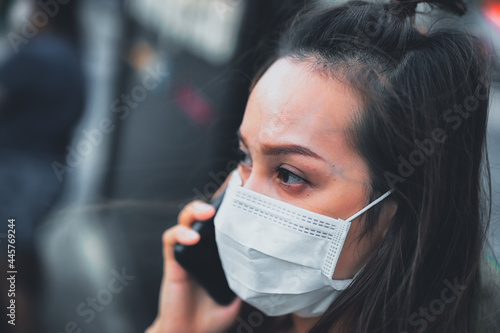 Young woman wearing surgical mask on street while using mobile phone. Portrait of young woman wearing a protective mask to prevent germs