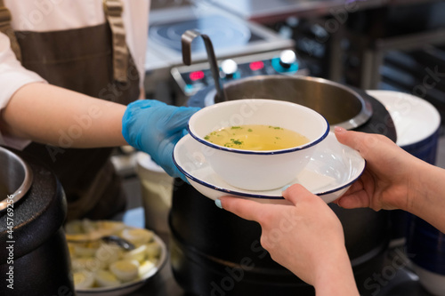 Distribution of food in the dining room. Passing a plate of soup from hand to hand on the background of pots.