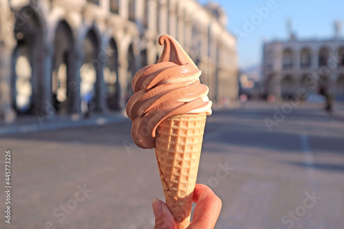 Delectable Chocolate and Vanilla Soft Serve Ice Cream in Hand against Blurry Vintage Buildings