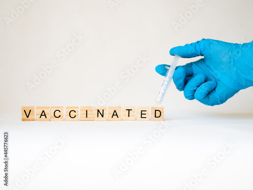 vaccinated - słowo ułożone z drewnianych kostek, strzykawka i ręka