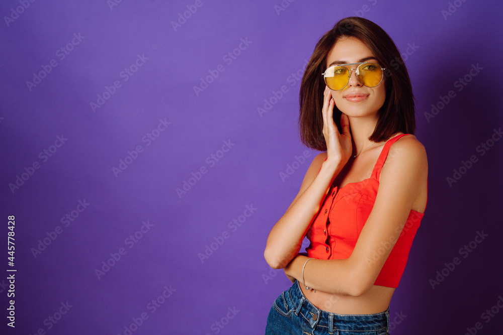 Beautiful young woman in a red top, skirt and yellow glasses posing on a purple background. Beauty and positive concept.