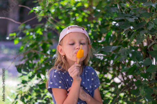 little girl, blonde, preschool girl stands in the park and eats popsicles