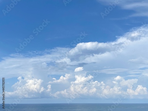 Sky clouds over sea water. Heaven clouds background. Divine blue skies, white clouds, sun rays. Beautiful cloudscape at sunny day. Spectacular cloudy sky on horizon over calm ocean.
