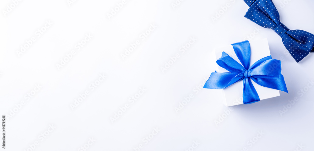Father day gift. White box with bow ribbon, blue bowtie or tie on light background. Concept of Fathers Day greeting card, copy space for text. Father day gift. White box with bow ribbon, blue bowtie or tie on light background. Concept of Fathers Day greeting card, copy space for text.