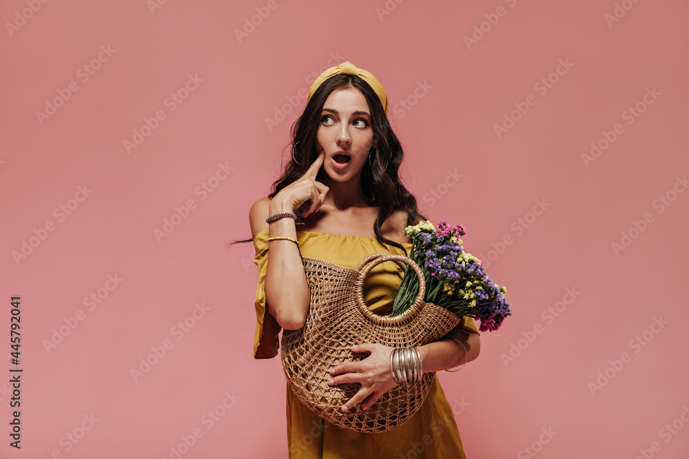Surprised charming girl with black curly hair with bracelets and earrings in stylish summer outfit looking away on pink backdrop.. Surprised charming girl with black curly hair with bracelets and earrings in stylish summer outfit looking away on pink backdrop..