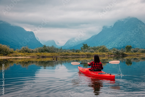 Adventure Caucasian Adult Woman Kayaking in Red Kayak surrounded by Canadian Mountain Landscape. Artistic Color Render. Taken in Widgeon Valley, Pitt Meadows, Vancouver, British Columbia, Canada.