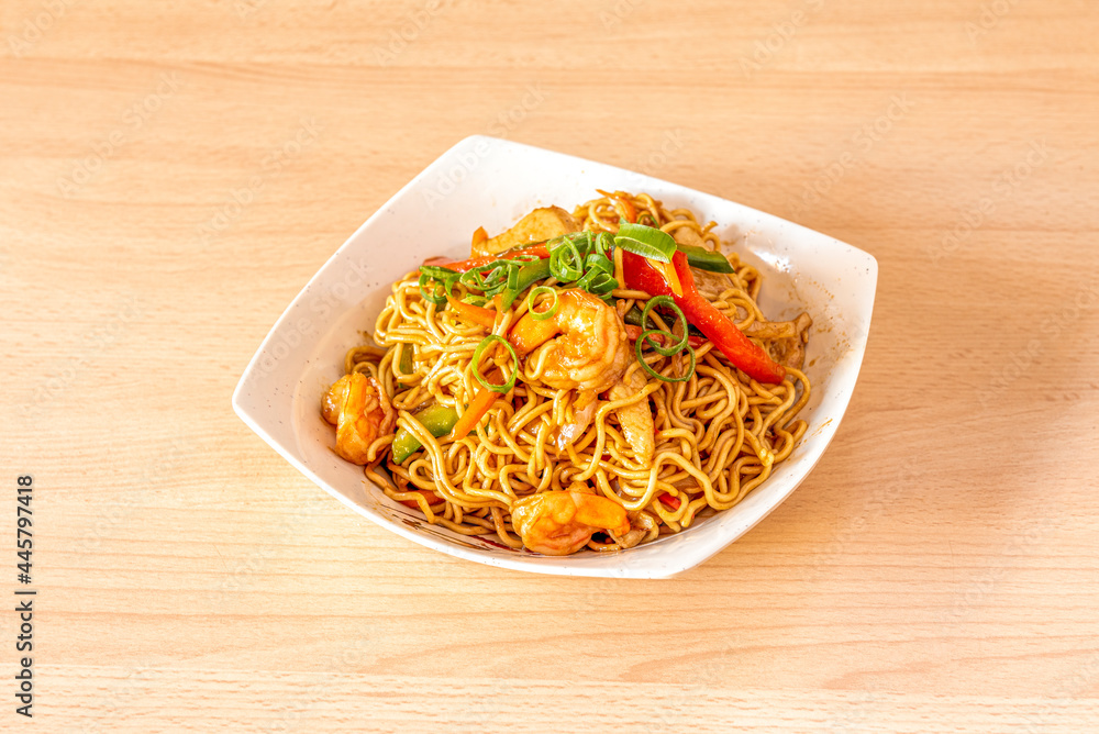 Yakisoba noodles with shrimp and peeled prawns, chopped chives and sauteed peppers and vegetables in white bowl and light wooden table Yakisoba noodles with shrimp and peeled prawns, chopped chives and sauteed peppers and vegetables in white bowl and light wooden table
