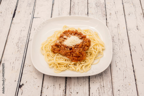 Cooked wheat flour pasta noodles accompanied by the everlasting Italian bolognese sauce on a white plate and with grated cheese on top