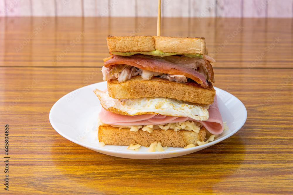 Super two-story sandwich with cheese, green sauce, fried bacon, shredded chicken, ham and fried egg with grilled sliced bread