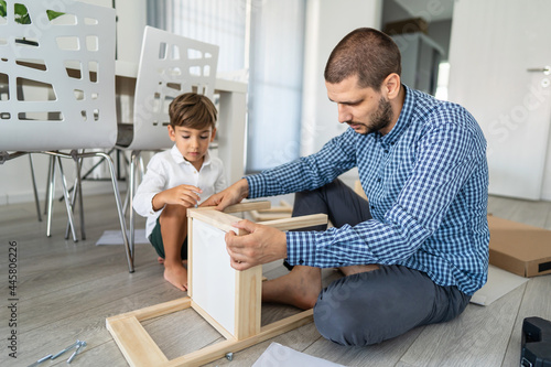 Small caucasian boy four years old and his father caucasian man putting together self assembly chair or table on the floor at home - little child assembling furniture fatherhood and craft concept
