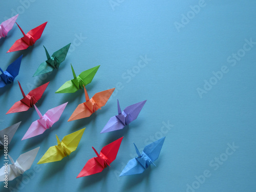 左下に集まるカラフルな折り鶴のグループと青背景のコピースペース