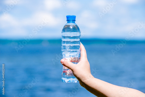 A girl holds a bottle of drinking water in her hand against a blue sky backgroun