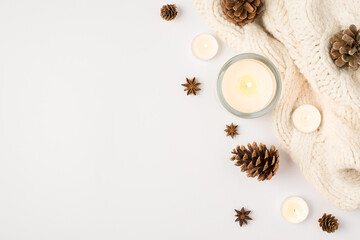 Top view photo of winter composition lighted candles white knitted sweater pine cones and anise on isolated white background with copyspace