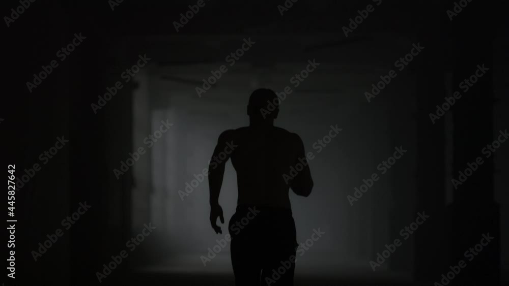 Fitness man running in dark corridor. Male jogger training in loft building