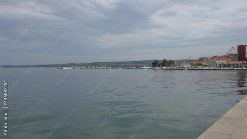 Walking on seafront walkway in seaside town Koper, Slovenia. Many boats and sailboats docked in harbor. Calm Adriatic Sea. POV walking on concrete promenade. Forward moving, wide angle Walking on seafront walkway in seaside town Koper, Slovenia. Many boats and sailboats docked in harbor. Calm Adriatic Sea. POV walking on concrete promenade. Forward moving, wide angle