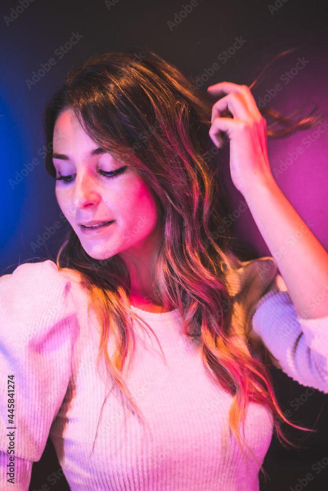 Urban portrait of a beautiful young woman looking at camera with pink and blue led lights on a black background Urban portrait of a beautiful young woman looking at camera with pink and blue led lights on a black background