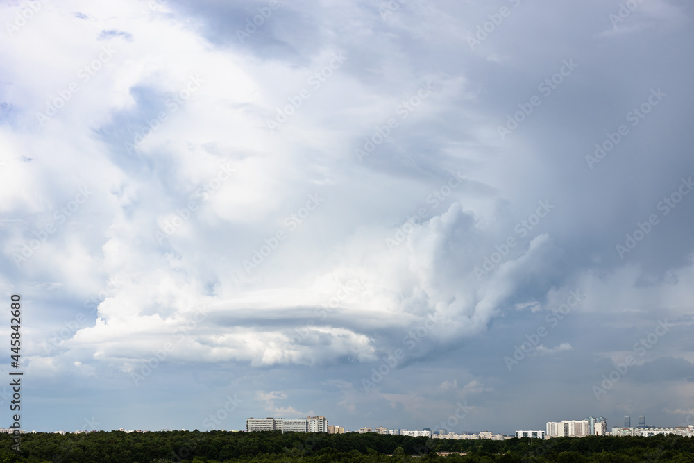 gray rainy clouds with whirls over city and forest