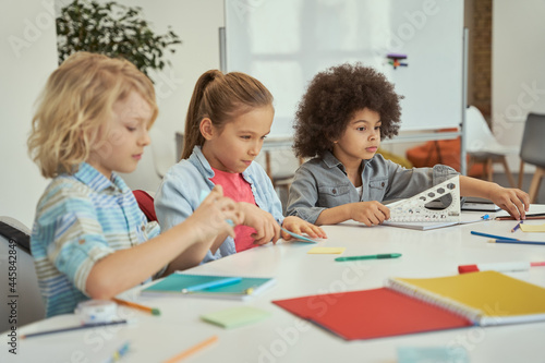 Cute diverse kids sitting together at the table while studying in elementary school classroom