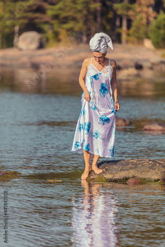 Fototapeta Naklejka Na Ścianę i Meble -  Young woman with a towel on her head at the sea. The lady walks on the water. The concept of summer outdoor recreation, relaxation. good weather