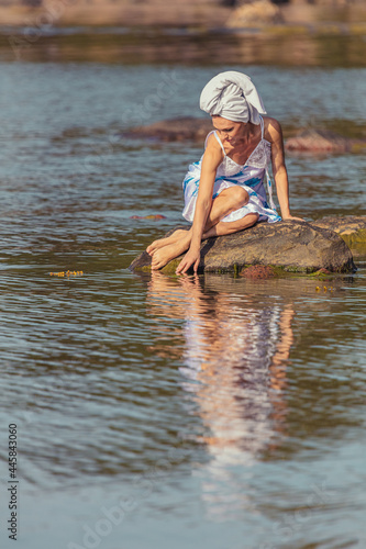 Young woman with a towel on her head at the sea. The lady touches the water with her hands. The concept of summer outdoor recreation, relaxation. good weather