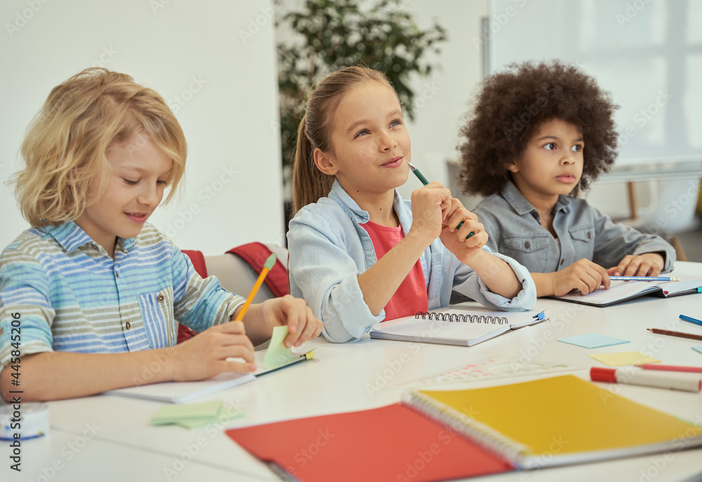 Education is key. Lovely diverse kids studying and making notes while sitting together at the table in elementary school classroom Education is key. Lovely diverse kids studying and making notes while sitting together at the table in elementary school classroom
