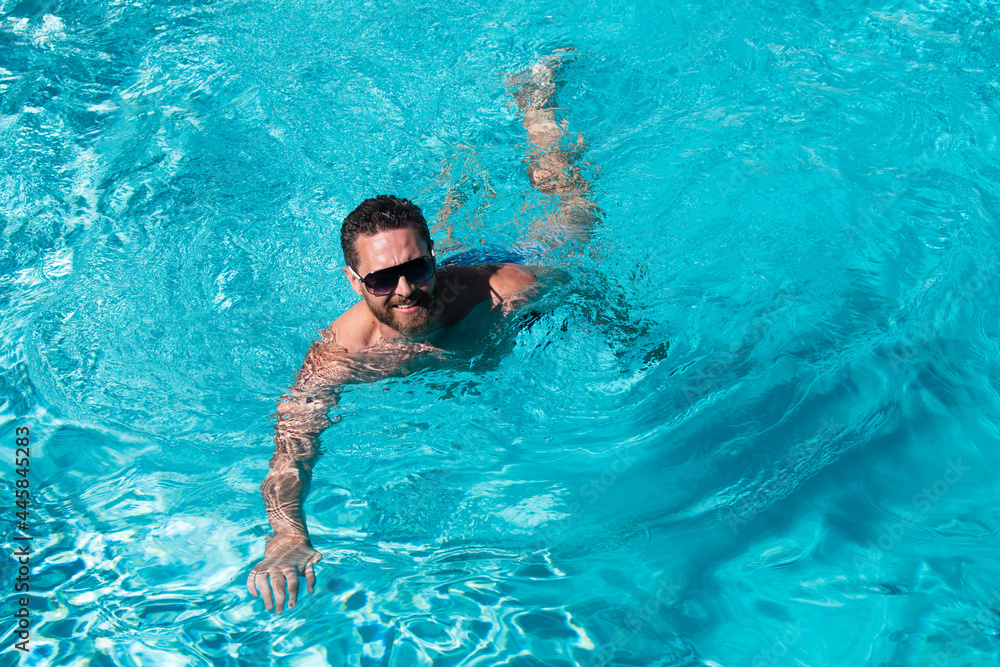 Man at summer vacation. Guy in sunglasses swimming in pool. Summertime pool resort.