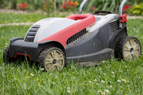 An old plastic electric lawn mower stands on a mowed lawn