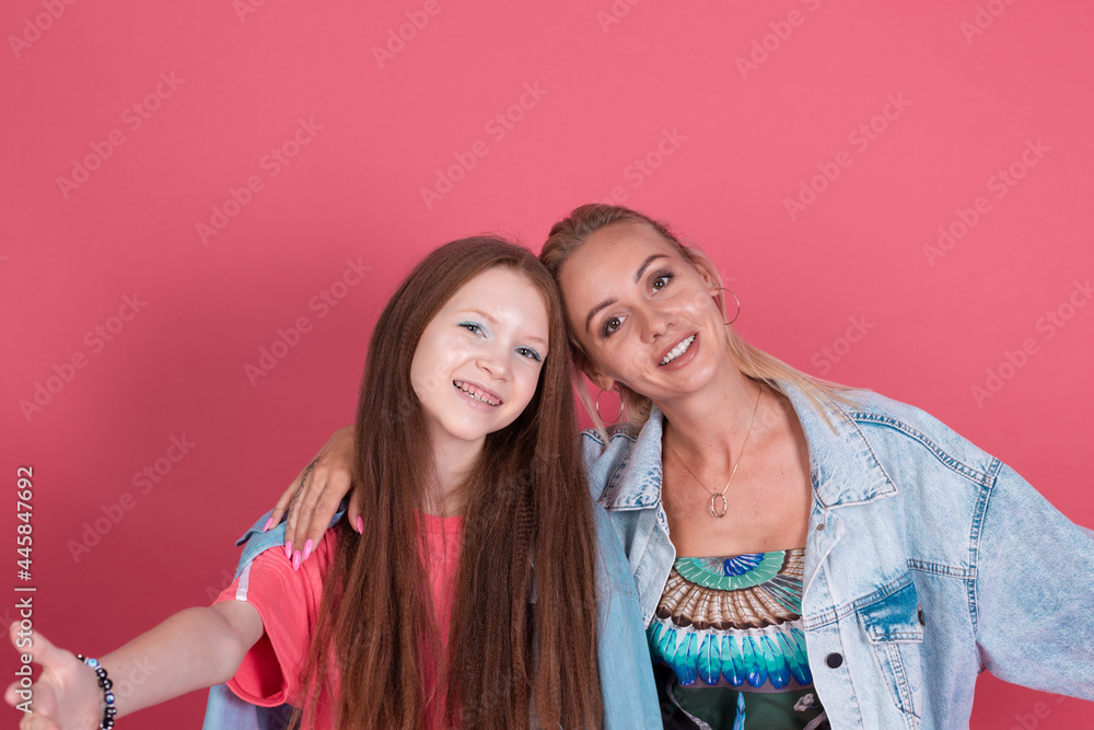 Modern mom and daughter in denim jackets on terracotta background hugging and smiling Modern mom and daughter in denim jackets on terracotta background hugging and smiling