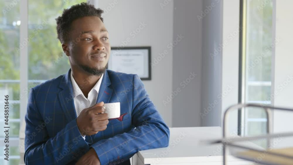 Happy african businessman taking break in office drinking coffee standing in window and daydreaming Happy african businessman taking break in office drinking coffee standing in window and daydreaming