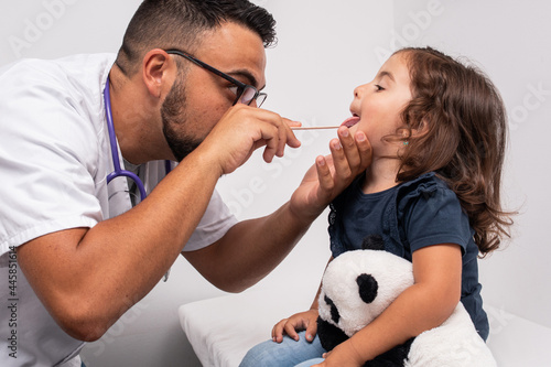 Pediatric doctor examining the throat of his little patient