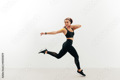 Asian woman look back while jumping and running against a white wall